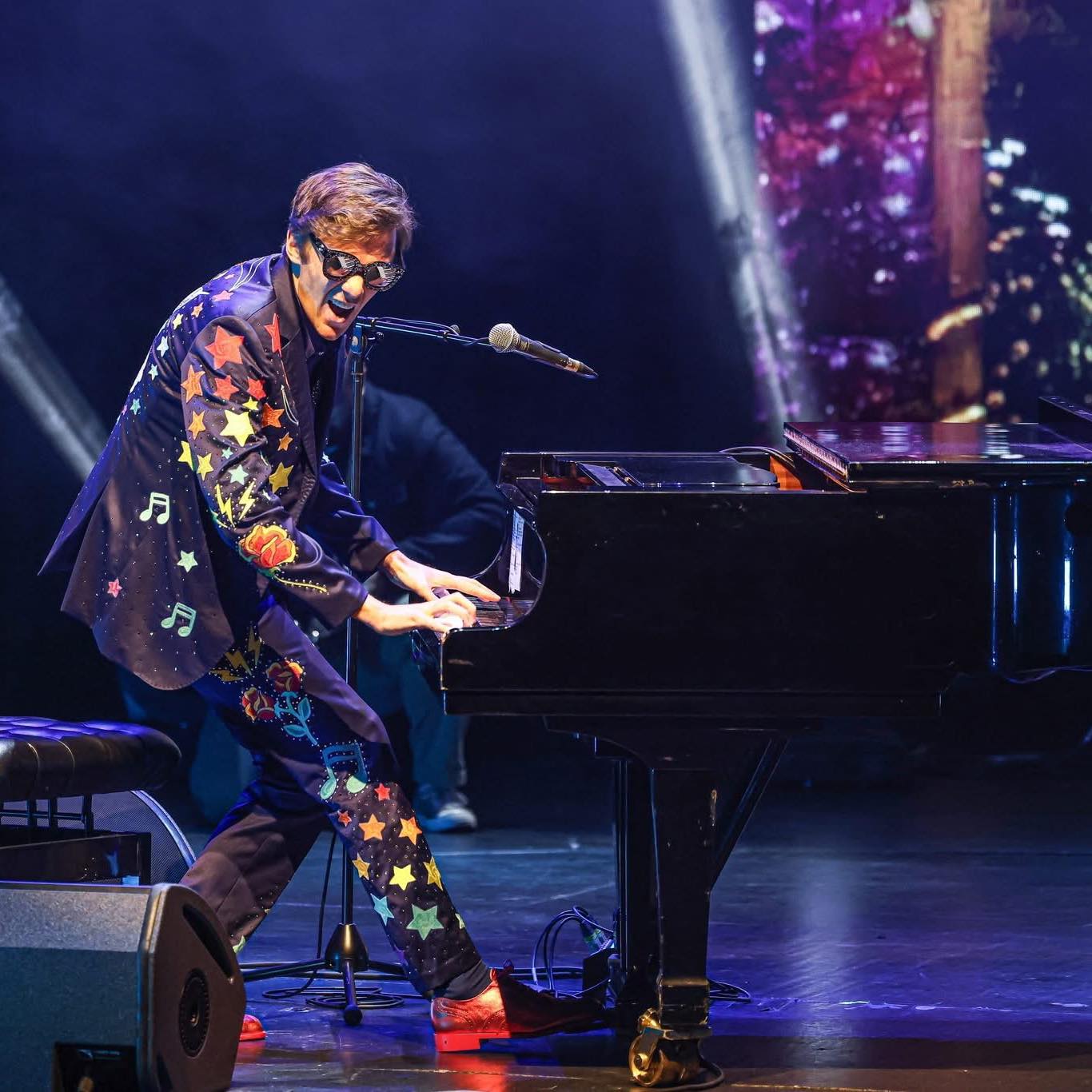 Sir El Tom live at the piano in a star-and-rose embroidered suit